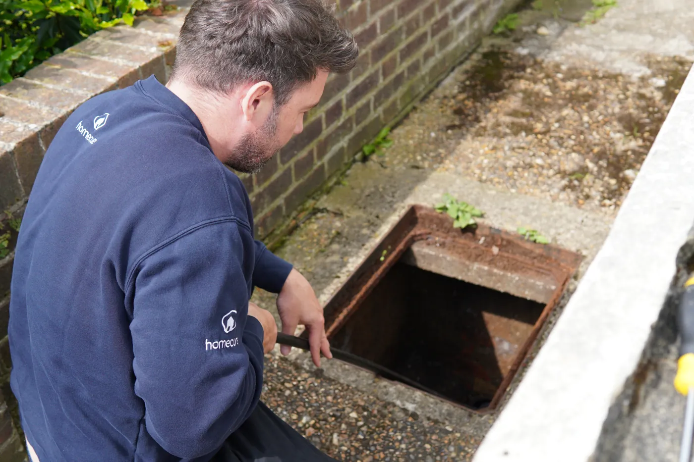 A Homecure engineer rodding an open drain inspection chamber