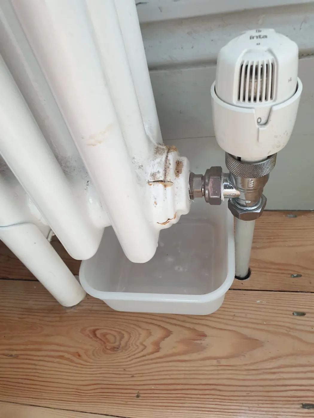 A radiator valve leaking water into a tray on a wooden floor